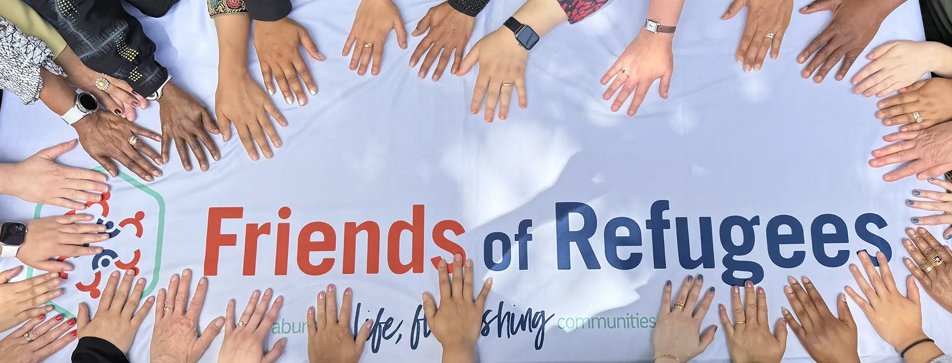 staff-hands A circle of hands touching a banner with the Friends of Refugee's logo.