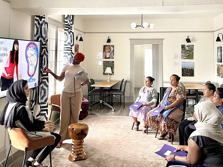 An Embrace Refugee Birth instructor gestures to an instructional slide while another instructor and a group of expecting mothers look on during a Healthy Moms class.