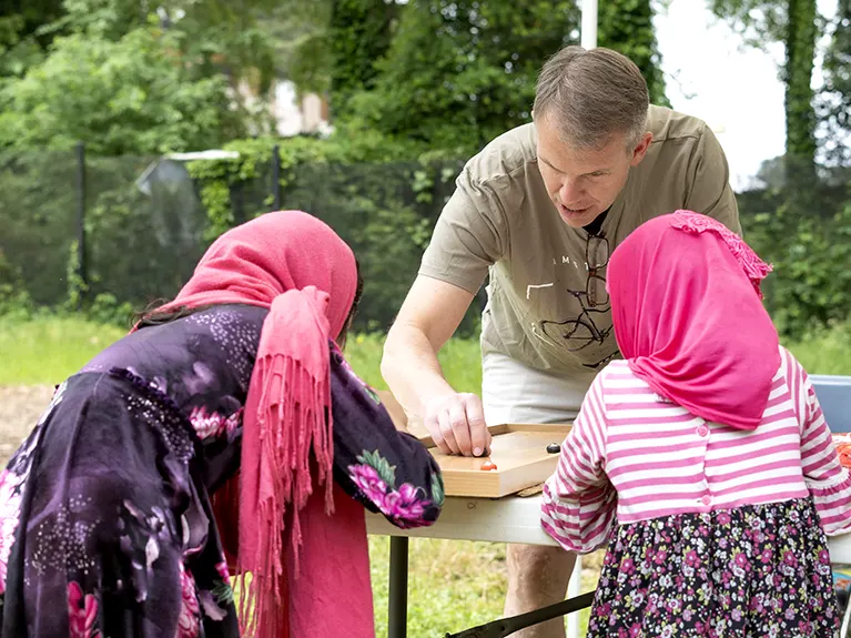 A volunteer plays a tabletop game with two young refugee girls at a Friends of Refugees event.
