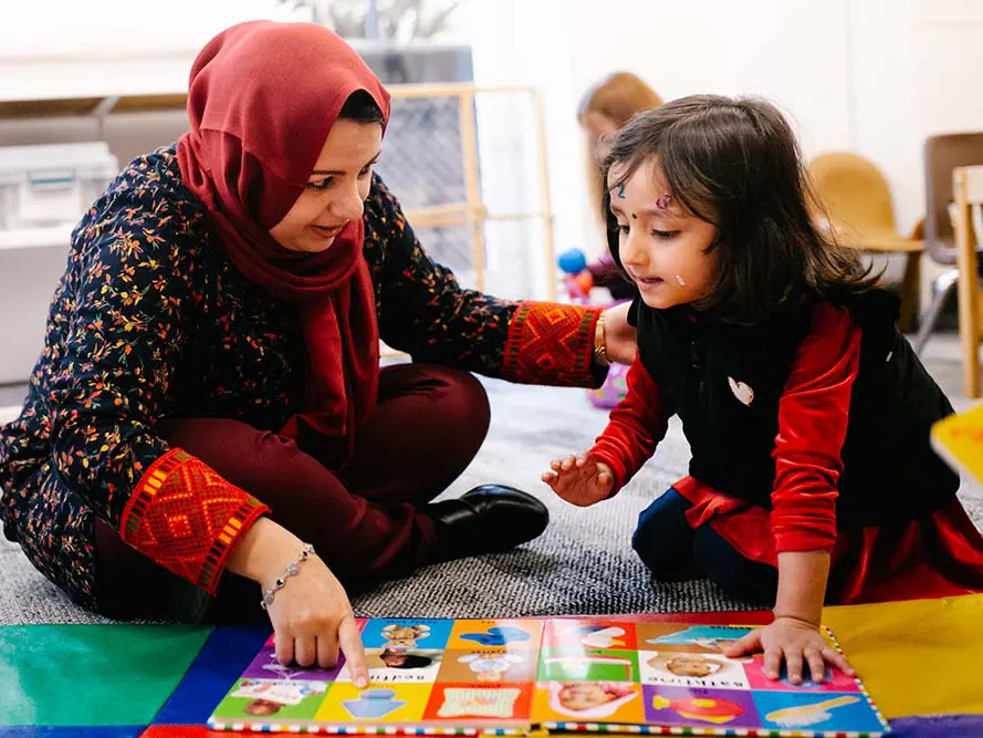 A refugee mother and her young daughter sit on the floor reading a picture book during a Refugee Family Literacy class.